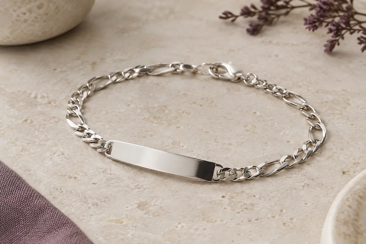 Bracelet argenté à chaîne Figaro et plaque lisse personnalisable posé sur une pierre claire