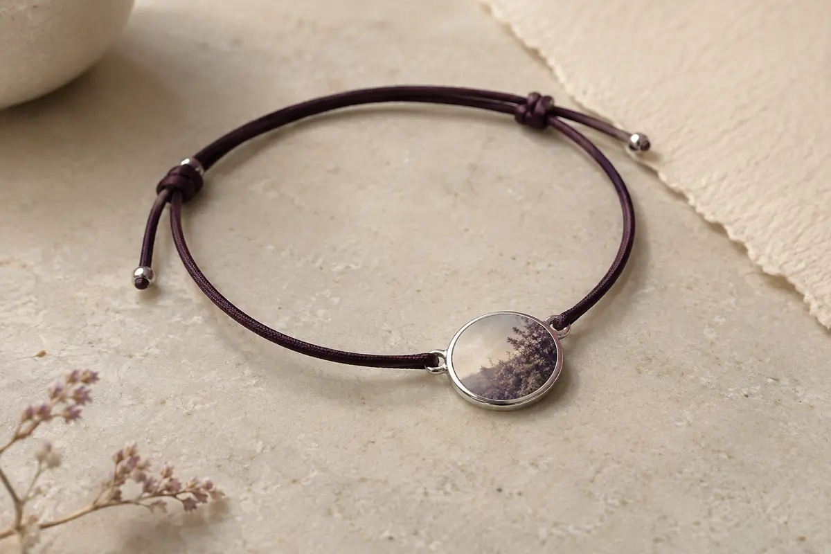 Bracelet à cordon réglable avec pendentif rond argenté en acier inoxydable posé sur une pierre claire.