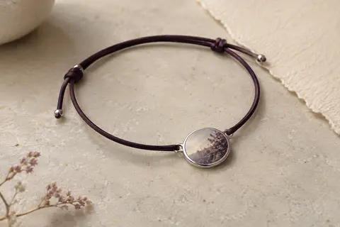 Bracelet à cordon réglable avec pendentif rond argenté en acier inoxydable posé sur une pierre claire.