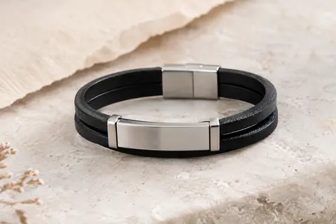 Bracelet homme noir à double lanière avec plaque argentée personnalisable, posé sur une pierre claire