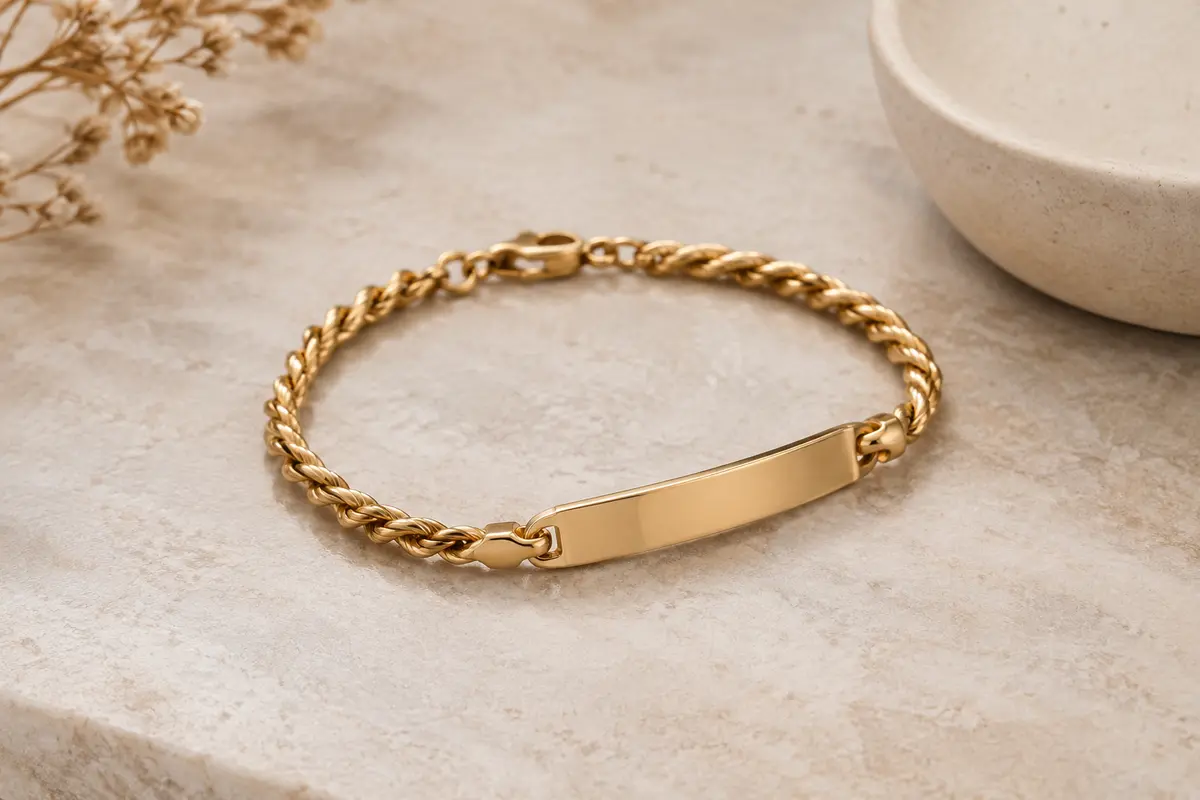 Gourmette dorée à bracelet torsadé et plaque lisse posée sur une pierre claire
