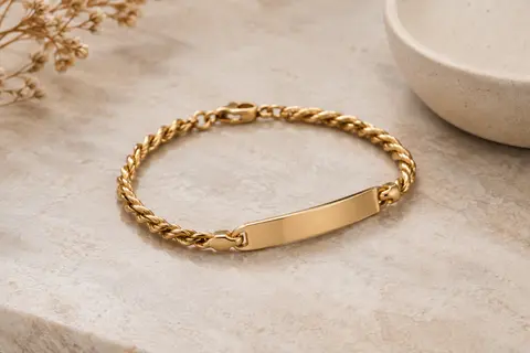 Gourmette dorée à bracelet torsadé et plaque lisse posée sur une pierre claire