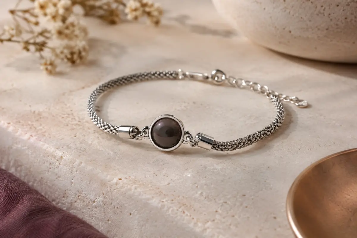 Bracelet photo à l’apparence argentée posé sur une pierre claire, avec sa pierre centrale circulaire.