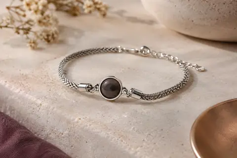 Bracelet photo à l’apparence argentée posé sur une pierre claire, avec sa pierre centrale circulaire.