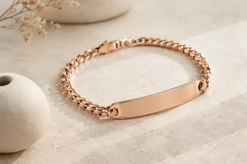 Bracelet médical à plaque lisse et maille métallique or rose posé sur une pierre claire
